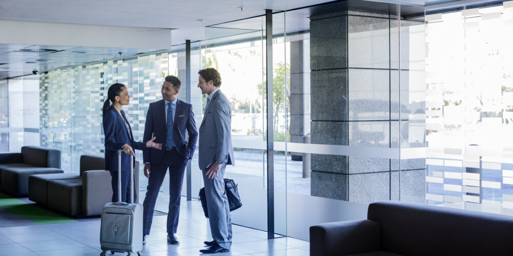 Full length of businesspeople with luggage discussing at office lobby